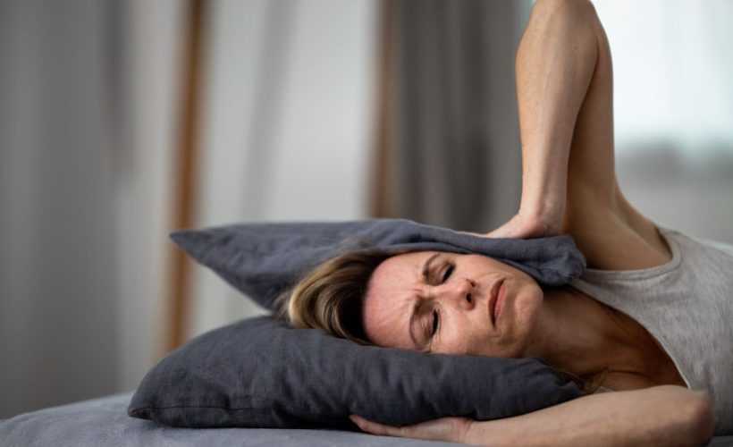 Sleepless lady covering ears with pillow. Noisy neighbors